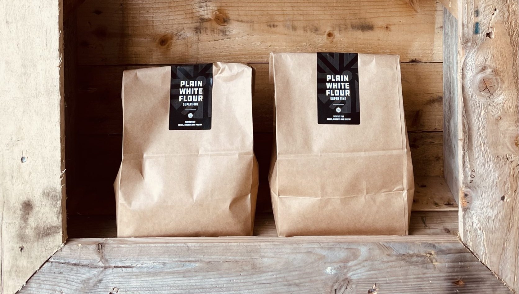 Two bags of Norfolk & Better Plain White Flour, super fine, on a rustic wooden shelf