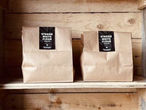 Two bags of Norfolk & Better Strong White Flour, super fine, on a rustic wooden shelf
