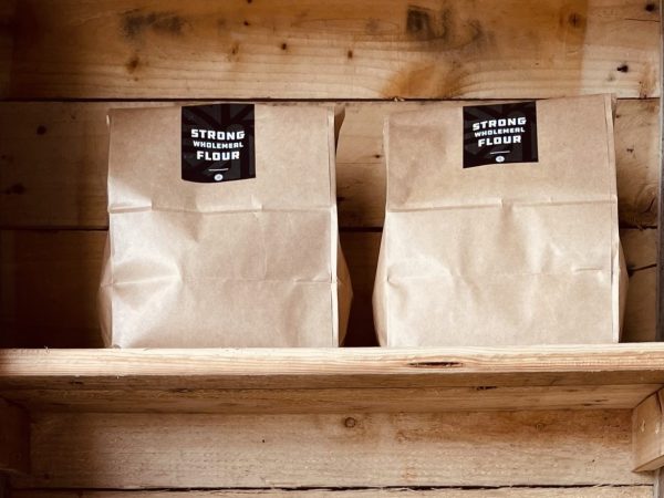 Two bags of Norfolk & Better Strong Wholemeal Flour on a rustic wooden shelf